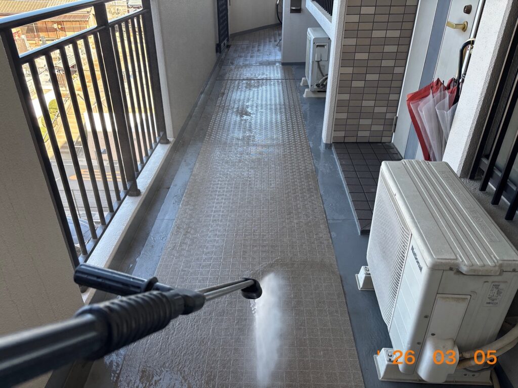 共用廊下の床面を高圧洗浄機で勢いよく洗い流している様子