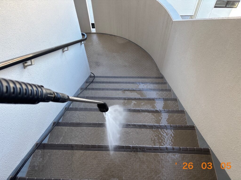 マンションの階段部分を高圧洗浄機で丁寧に清掃している様子