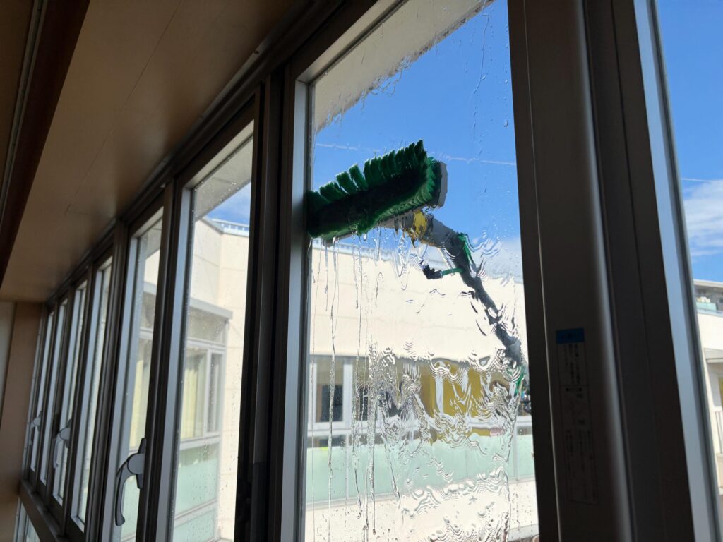 室内から見た窓ガラス清掃の様子。ウォーターポールのブラシから水がたっぷりと流れ落ちている