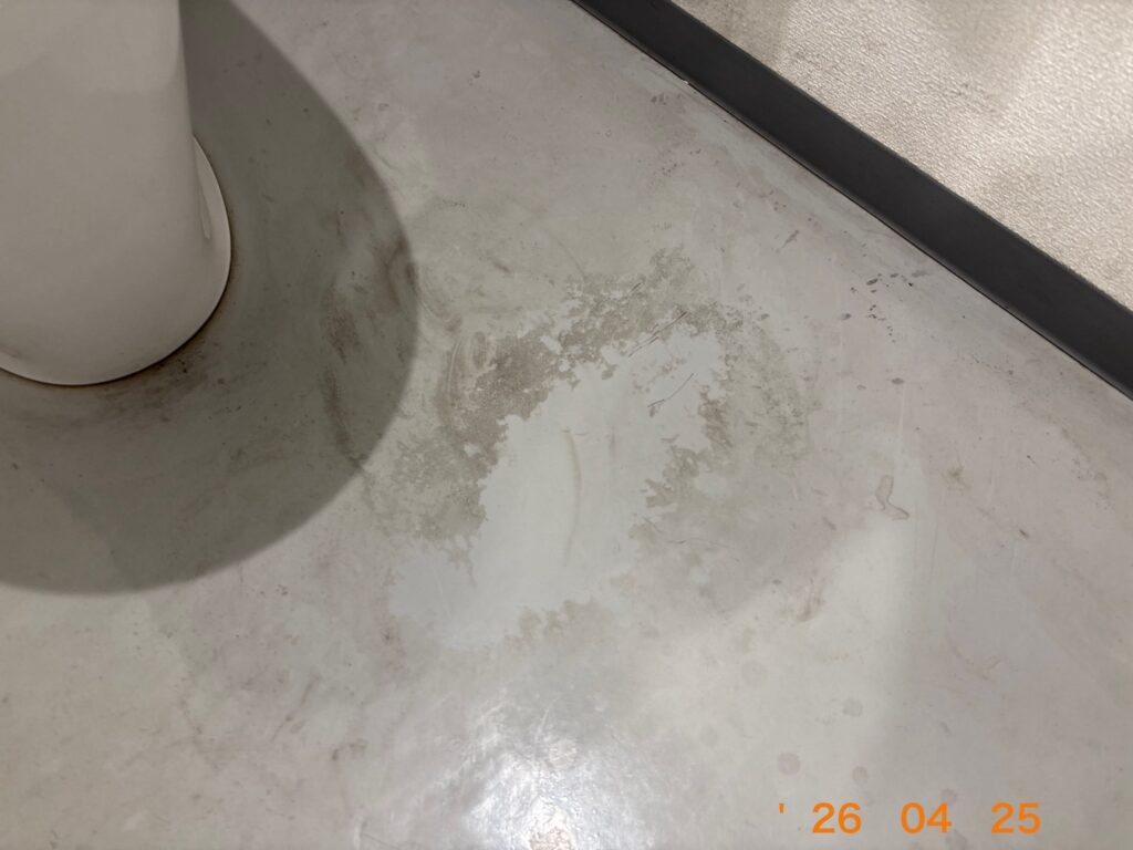 便器のすぐ横の床面に、何か液体を垂らしたような白く変色した跡が残っている様子