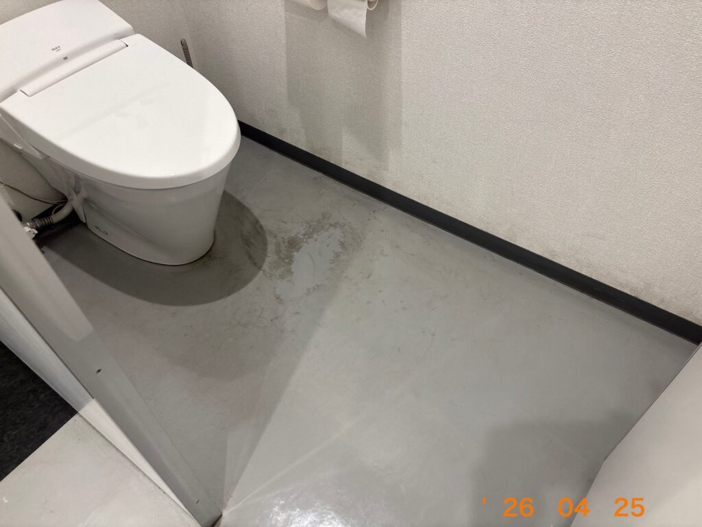 便器のすぐ横の床面に、何か液体を垂らしたような白く変色した跡が残っている様子