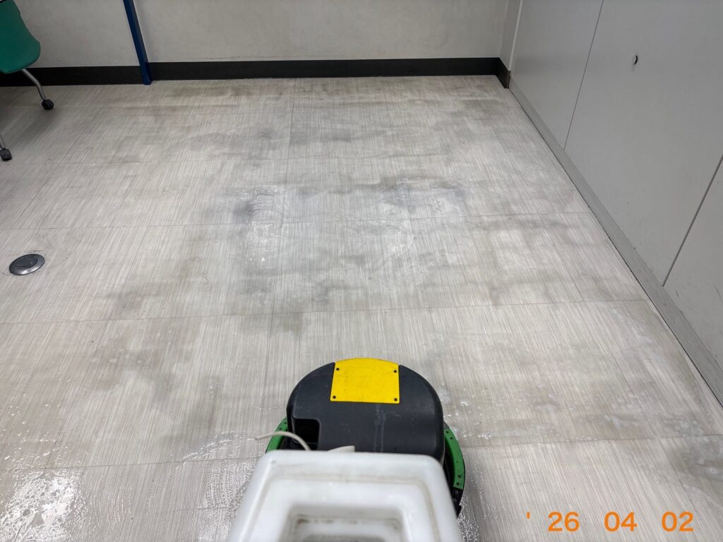 床用ポリッシャーを巧みに操り、廊下の古い汚れを丁寧に洗い落としている作業風景