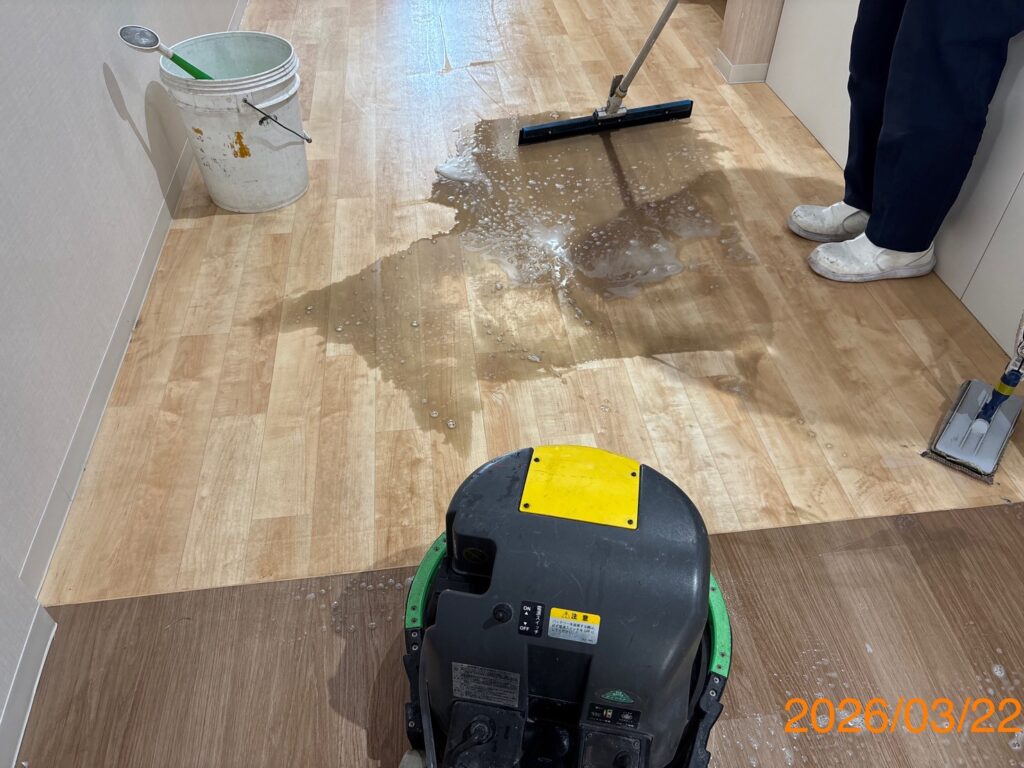 ポリッシャーを使用して床面を洗浄している様子。床から茶色く濁った汚水が浮き出ている