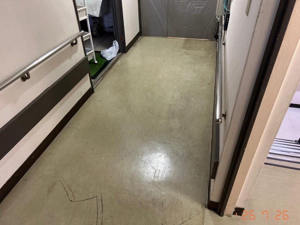 剥離作業中の床。ワックスと汚れが浮き、表面がまだらに黒ずんで見える状態。